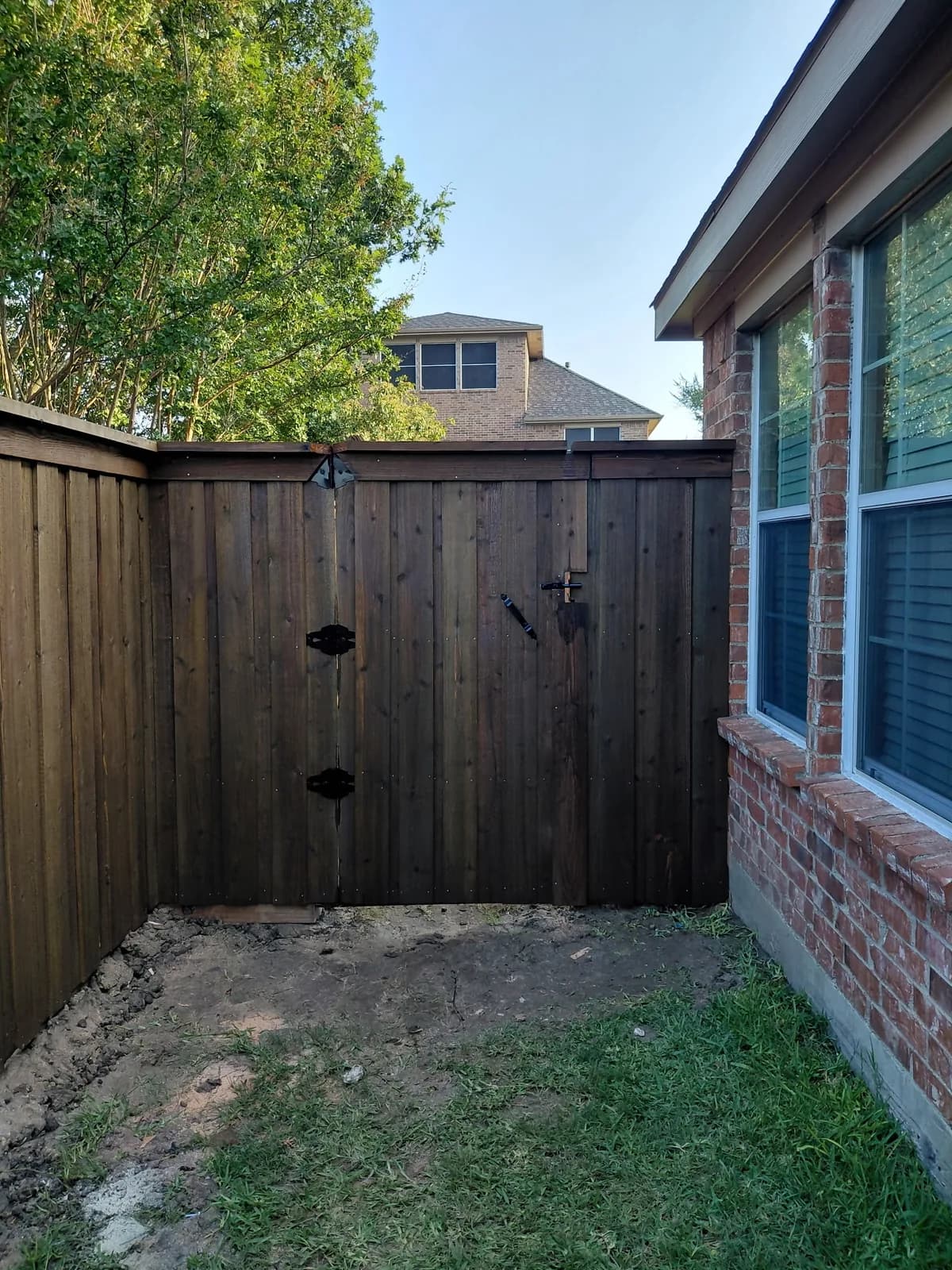 Cedar double gate with black strap hinges beside a brick home.