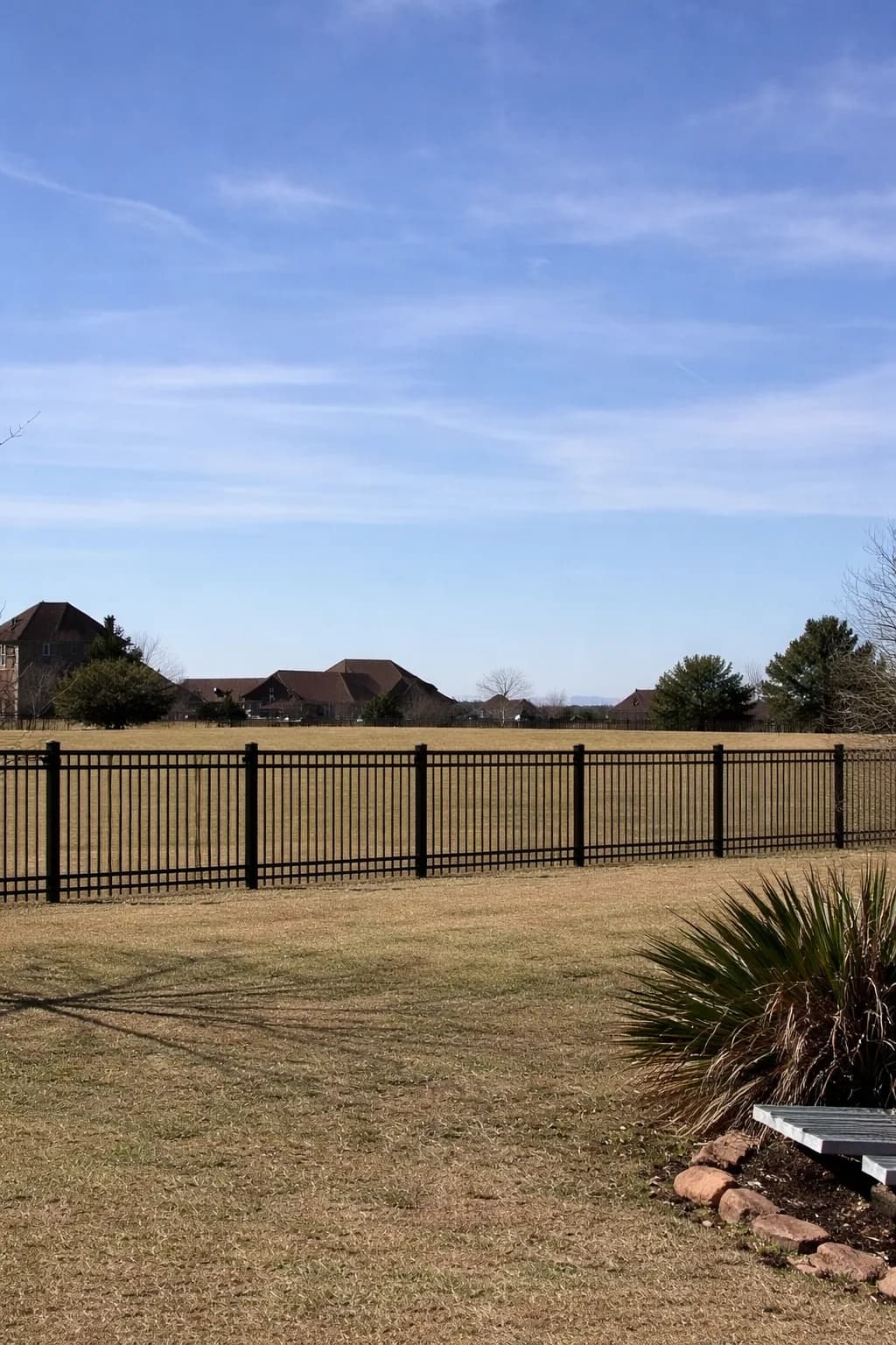 Black ornamental iron fence bordering an open field.