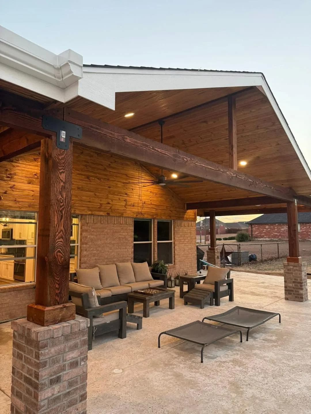Cedar-ceilinged patio cover on brick columns, lit at dusk.